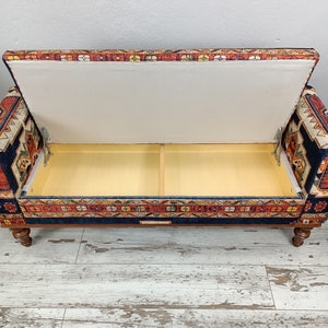 May include: A blue and red patterned storage ottoman with a hinged lid open, revealing a beige interior. The ottoman has turned wooden legs.
