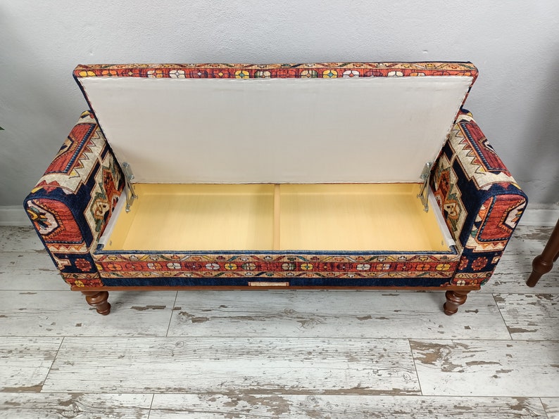 May include: A blue and red patterned storage ottoman with a hinged lid open, revealing a beige interior. The ottoman has turned wooden legs.