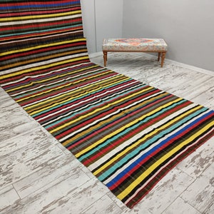 May include: A colorful striped rug with a variety of colors, including red, yellow, blue, green, and brown. The rug is laid out on a whitewashed wood floor.