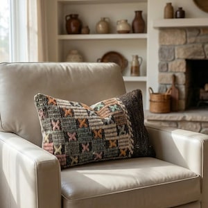 May include: Two decorative throw pillows on a cream-colored leather armchair. The pillows feature a patchwork design with various colors, including brown, green, orange, and pink. The background includes a fireplace and shelves with pottery.