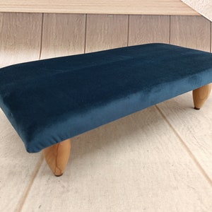 Può includere: Uno sgabello in velluto blu scuro con quattro gambe in legno.