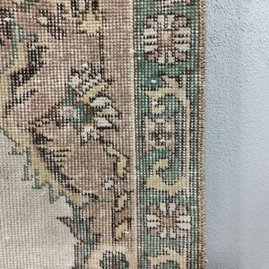 May include: Close-up of the edge of a beige rug with a green and brown floral pattern.