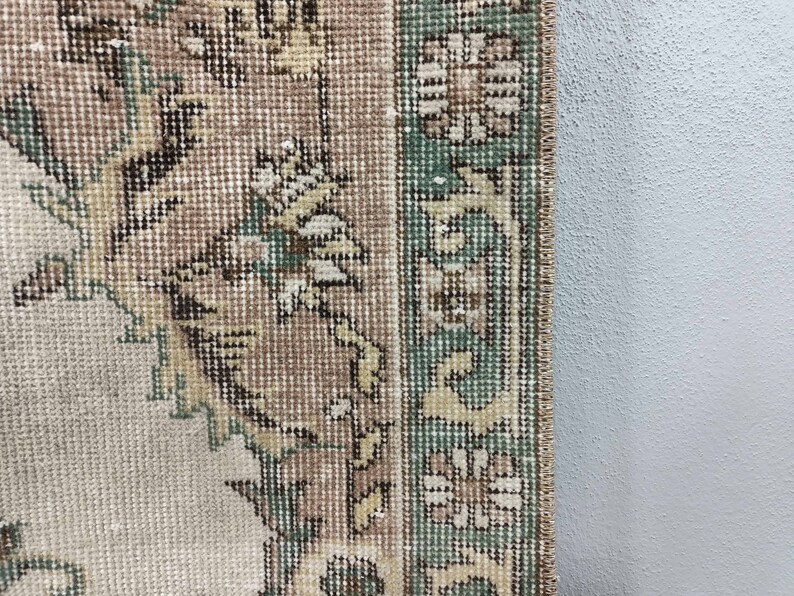 May include: Close-up of the edge of a beige rug with a green and brown floral pattern.