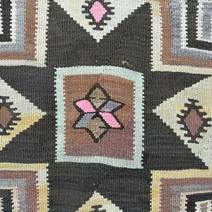 May include: A close-up of a woven rug with a geometric pattern in shades of brown, gray, white, and pink. The rug features a central star shape with a smaller star inside.