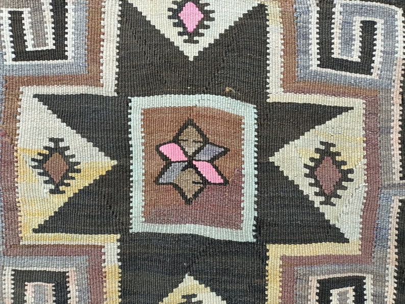 May include: A close-up of a woven rug with a geometric pattern in shades of brown, gray, white, and pink. The rug features a central star shape with a smaller star inside.