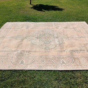 May include: A light pink rug with a faded, intricate floral pattern in shades of gray. The rug has a border with a similar pattern.