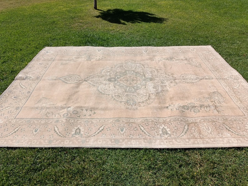 May include: A light pink rug with a faded, intricate floral pattern in shades of gray. The rug has a border with a similar pattern.