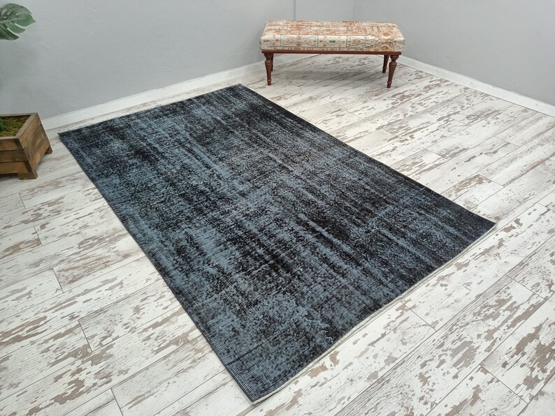 May include: A blue and black distressed rug with a faded, vintage look. The rug has a rectangular shape and is laid out on a whitewashed wood floor.