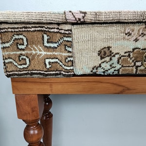 Op de afbeelding: Een houten tafel met een lade en een blad bedekt met een patchwork van kleurrijke tapijten. De lade heeft een messing ringgreep.