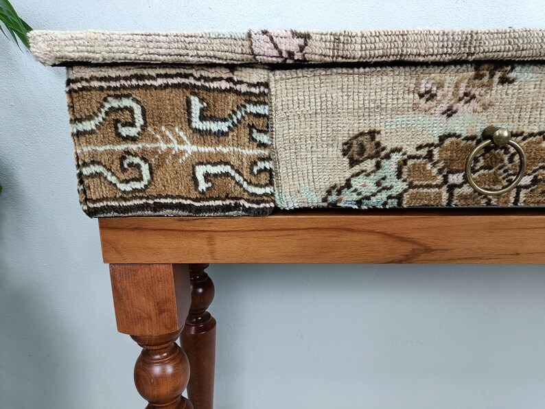 Op de afbeelding: Een houten tafel met een lade en een blad bedekt met een patchwork van kleurrijke tapijten. De lade heeft een messing ringgreep.