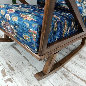 a wooden rocking chair with a blue and white floral patterned cushion, placed on a white wooden floor.