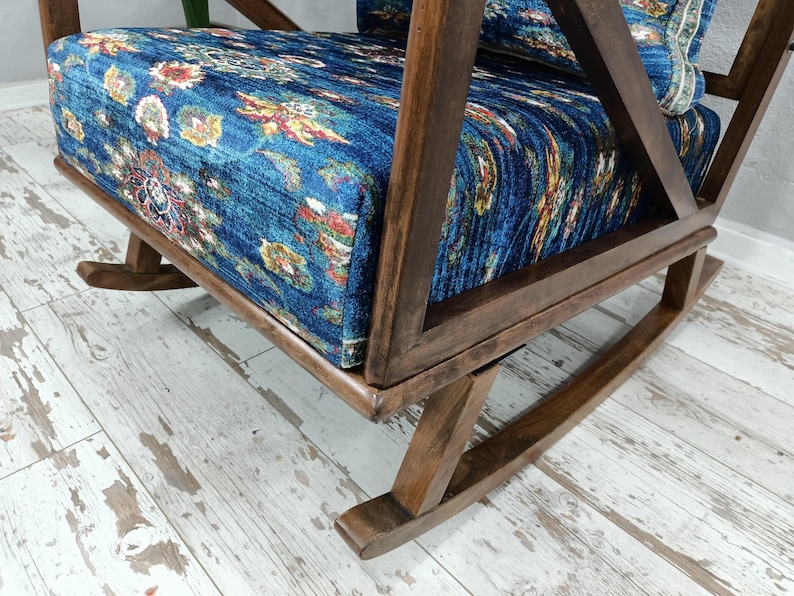a wooden rocking chair with a blue and white floral patterned cushion, placed on a white wooden floor.