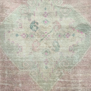 May include: A vintage rug with a faded pink and cream colour scheme. The rug features a central diamond-shaped design with intricate floral patterns in shades of pink and green.