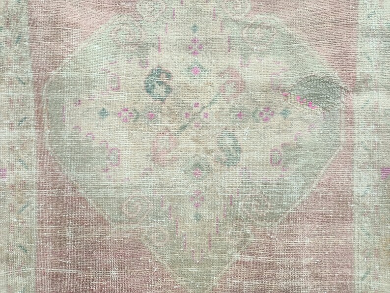 May include: A vintage rug with a faded pink and cream colour scheme. The rug features a central diamond-shaped design with intricate floral patterns in shades of pink and green.