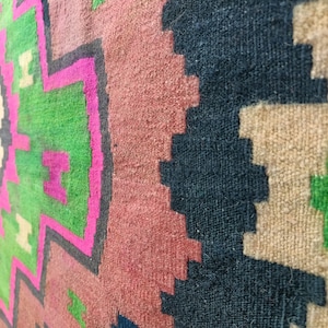 Puede incluir: Primer plano de una alfombra tejida colorida con patrones geom&eacute;tricos en tonos de rosa, verde, negro y beige.
