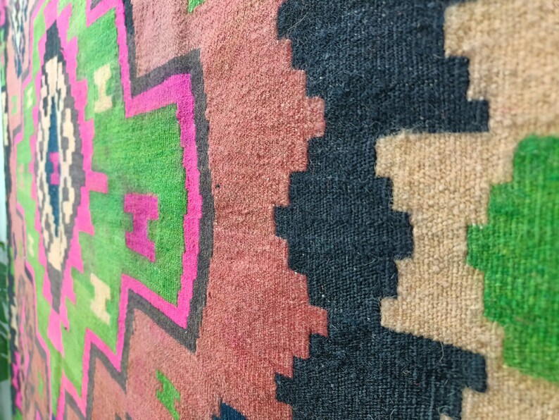 Puede incluir: Primer plano de una alfombra tejida colorida con patrones geom&eacute;tricos en tonos de rosa, verde, negro y beige.