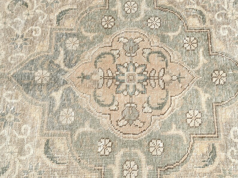 May include: A vintage rug with a beige and green color scheme. The rug features a central medallion with a floral design. The rug has a distressed look, with some areas showing wear and tear.