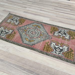 以下が含まれることがあります： 幾何学模様のピンクとグリーンのヴィンテージラグ。ラグは色あせていて、ウール製です。