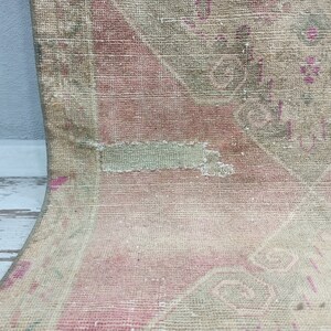 May include: A vintage rug with a faded pink and green floral pattern. The rug has a worn and distressed look, with some areas of the fabric missing.