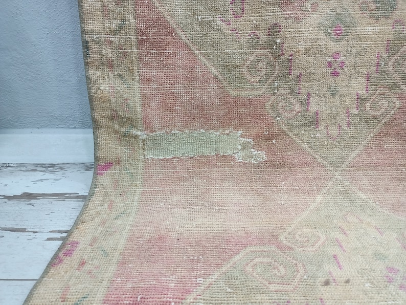 May include: A vintage rug with a faded pink and green floral pattern. The rug has a worn and distressed look, with some areas of the fabric missing.