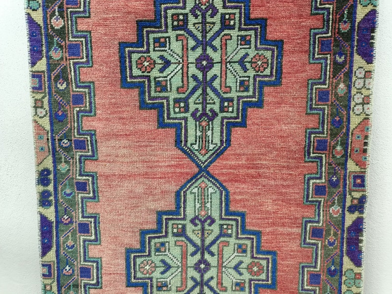 May include: A red runner rug with a geometric pattern in shades of blue, green, and pink. The rug has a fringed edge.