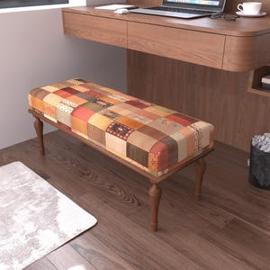 May include: A rectangular bench featuring a patchwork fabric seat with various square patterns in shades of orange, brown, red, and beige. The bench is supported by four turned wooden legs with a dark brown finish, providing a stable base.