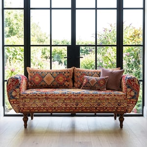 Könnte beinhalten: Ein Sofa mit einem farbenfrohen Muster in Rot, Blau und Gold. Das Sofa hat einen Holzrahmen und gedrechselte Beine. Mehrere Kissen in passenden Farben und Mustern sind auf dem Sofa angeordnet.