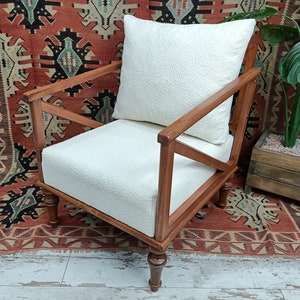 May include: A white armchair with a white cushion and wooden frame. The chair is sitting on a red and black patterned rug.