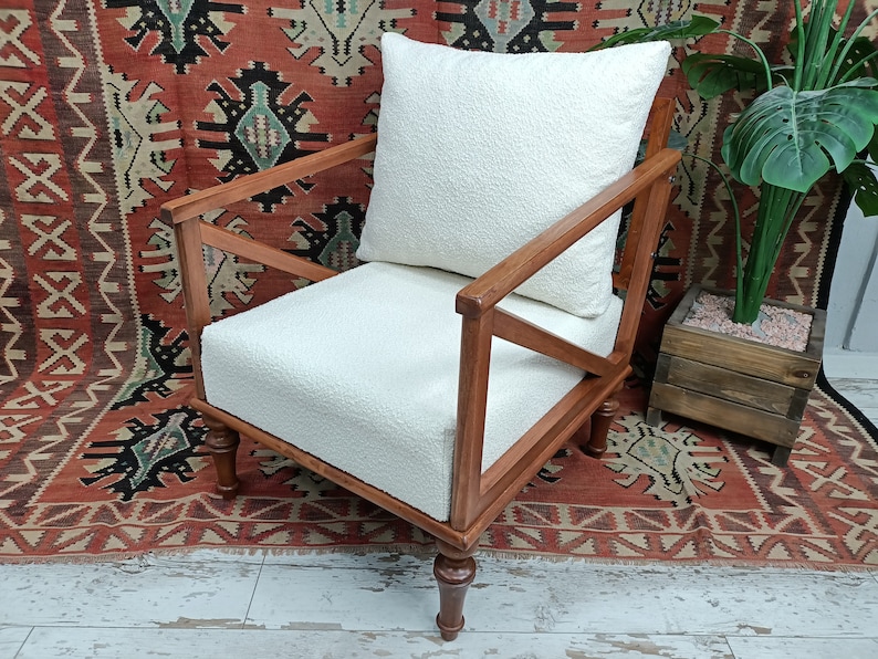 May include: A white armchair with a white cushion and wooden frame. The chair is sitting on a red and black patterned rug.