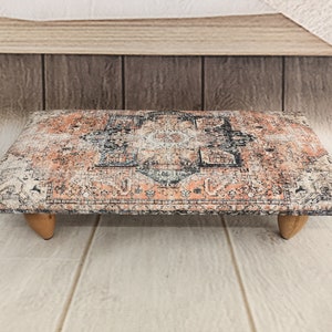 May include: A rectangular wooden tray with a patterned design resembling an oriental rug. The tray has four wooden legs and is painted in shades of pink, black, and white.