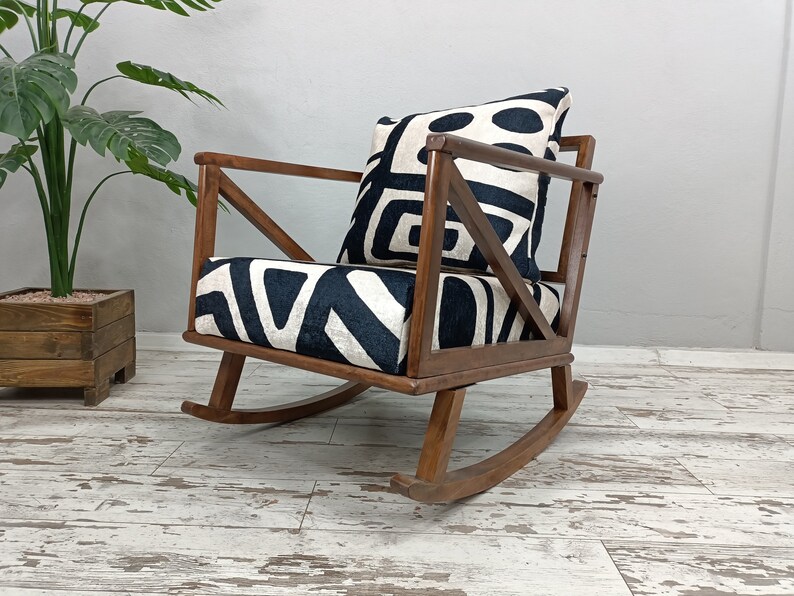 May include: A wooden rocking chair with a black and white geometric patterned cushion. The chair has a unique X-shaped design on the back.