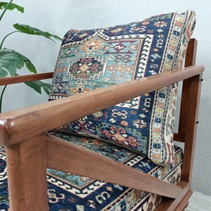 Puede incluir: Un sill&oacute;n de madera con un coj&iacute;n estampado en azul y rojo. La silla tiene un marco de madera oscura y un asiento de aspecto c&oacute;modo.