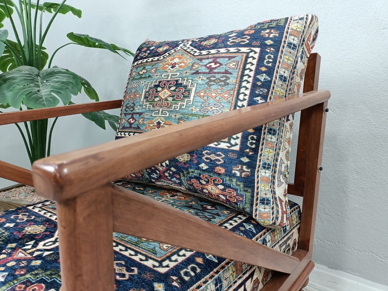 Puede incluir: Un sill&oacute;n de madera con un coj&iacute;n estampado en azul y rojo. La silla tiene un marco de madera oscura y un asiento de aspecto c&oacute;modo.