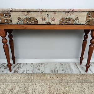 Op de afbeelding: Een houten consoletafel met twee laden en gedraaide poten. De bovenkant van de tafel is bedekt met een gepatenteerde stof in roze, bruin en beige kleuren.