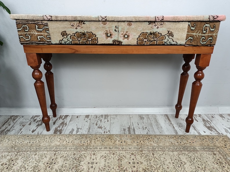 Op de afbeelding: Een houten consoletafel met twee laden en gedraaide poten. De bovenkant van de tafel is bedekt met een gepatenteerde stof in roze, bruin en beige kleuren.