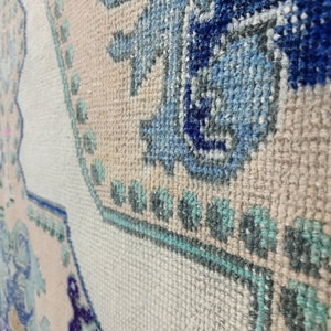 K&ouml;nnte beinhalten: Nahaufnahme eines cremefarbenen Teppichs mit einem blauen, gr&uuml;nen und rosafarbenen Blumenmuster. Der Teppich hat eine gewebte Textur und besteht aus weichen Fasern.
