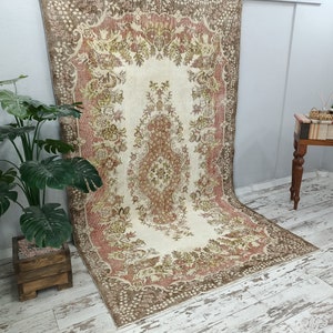 Op de afbeelding: Een vintage tapijt met een bloemenpatroon in tinten bruin, beige en roze. Het tapijt heeft een centraal medaillon en een rand met een herhalend ontwerp.