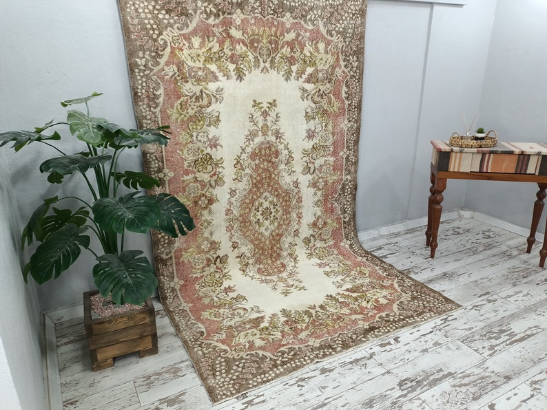 Op de afbeelding: Een vintage tapijt met een bloemenpatroon in tinten bruin, beige en roze. Het tapijt heeft een centraal medaillon en een rand met een herhalend ontwerp.