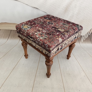 May include: A square ottoman with a red, brown, and cream patterned fabric top and four wooden legs.