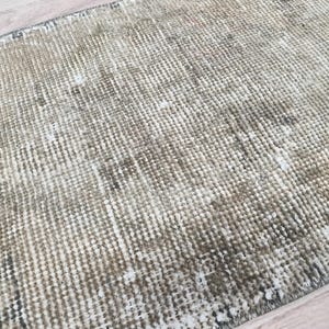 May include: A close-up of a beige and brown woven rug with a subtle pattern. The rug has a distressed, vintage look and is made of natural fibres.
