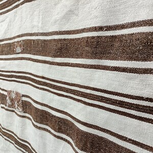 Puede incluir: Primer plano de un textil tejido con rayas marrones y blancas alternas. La tela tiene un aspecto texturizado, con peque&ntilde;as manchas irregulares de un color m&aacute;s claro. Las rayas son horizontales.