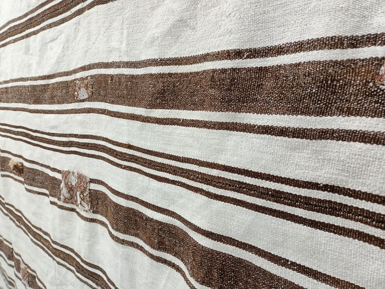Puede incluir: Primer plano de un textil tejido con rayas marrones y blancas alternas. La tela tiene un aspecto texturizado, con peque&ntilde;as manchas irregulares de un color m&aacute;s claro. Las rayas son horizontales.