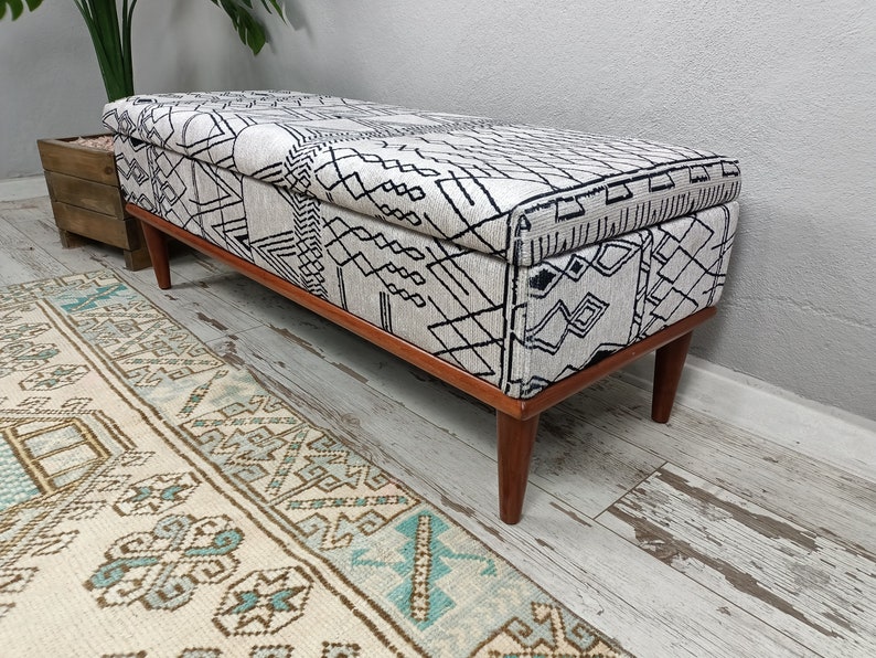 May include: A white and black patterned storage bench with wooden legs. The bench features a geometric design and is ideal for adding a touch of style to any room.