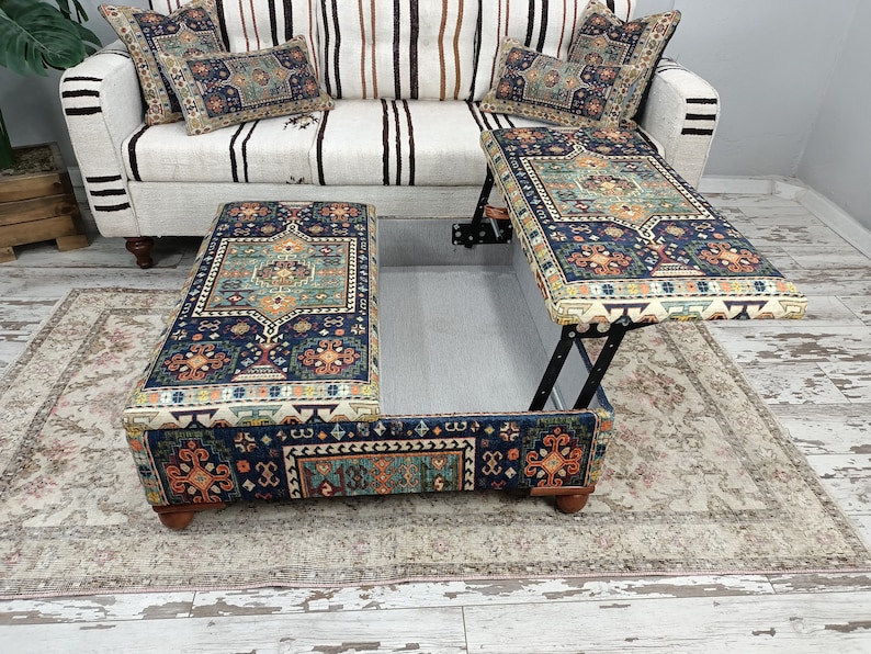 May include: A blue and orange patterned ottoman with a lift-top lid. The ottoman is open and the lid is propped up, revealing a storage compartment. The ottoman is sitting on a rug.