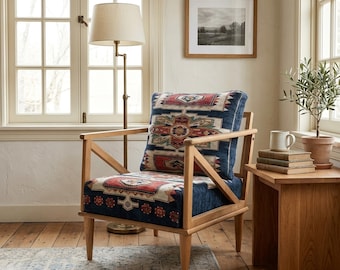 Könnte beinhalten: Ein Holzarmlehnstuhl mit hellem Rahmen und einem dunkelblauen Polstersitz sowie Rückenpolster mit geometrischem Muster in Rot, Weiß und Beige. Der Stuhl verfügt über angewinkelte Armlehnen und konische Beine für eine strukturierte Sitzgelegenheit.