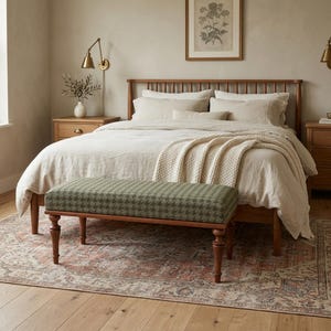 May include: A bedroom interior with a wooden bed, bedside tables, and a patterned bench. The bench has a green and white houndstooth design. A cream blanket is on the bed, and a rug with a faded pattern is on the floor. The room has a neutral color palette.