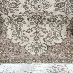 May include: A vintage rug with a cream background and a floral pattern in shades of brown and green. The rug has a fringed edge.