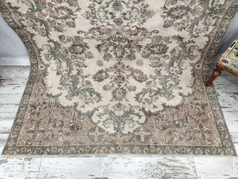 May include: A vintage rug with a cream background and a floral pattern in shades of brown and green. The rug has a fringed edge.