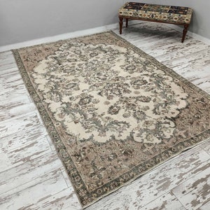 May include: A vintage cream-coloured rug with a floral pattern in shades of brown and green. The rug has a distressed look and is perfect for adding a touch of vintage charm to any room.