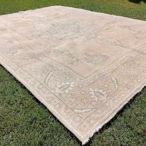 May include: A light beige rug with a floral pattern in a lighter shade of beige. The rug has a fringed edge.